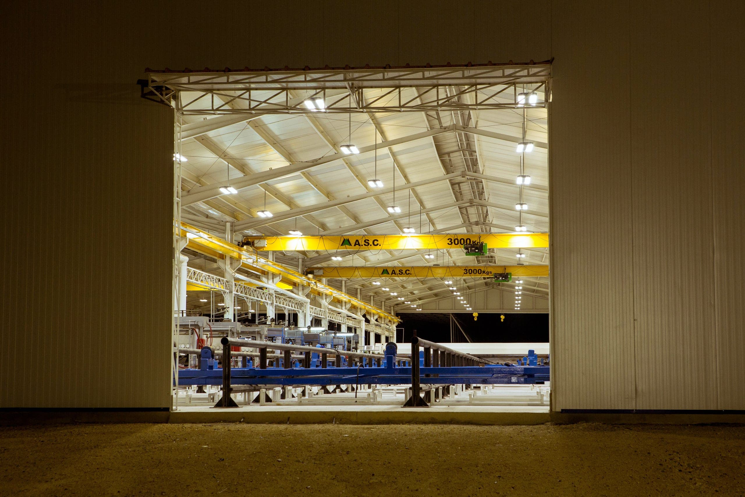 At night, through the open door: the lit hall, cranes and transfer tables.
