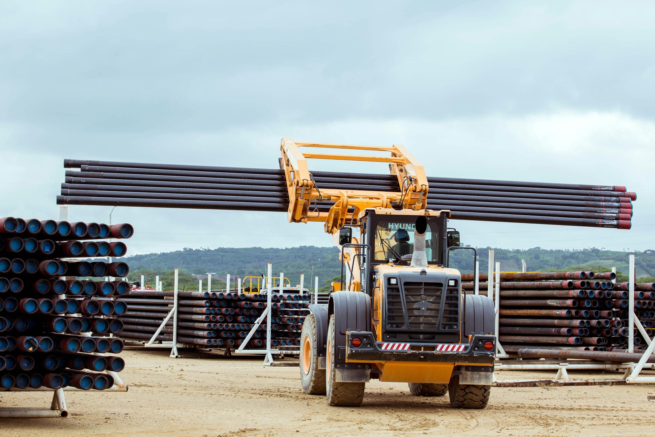 A loader carries a long bundle of liners between the stacks.